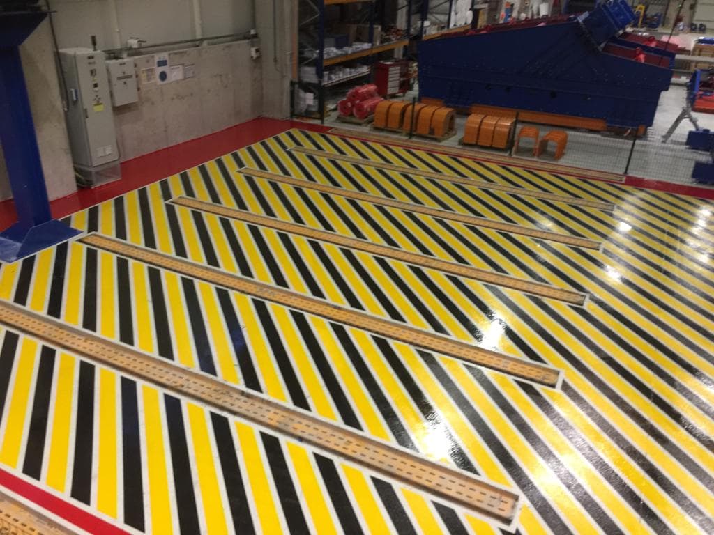 Üretim alanında sarı-siyah tehlike şeritleri ve kırmızı bordürle işaretlenmiş zemin